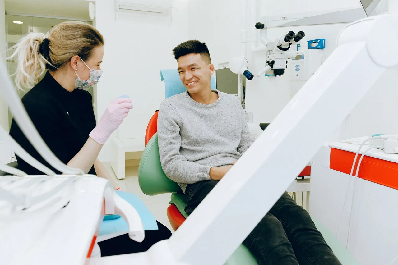 A dentist chatting with a smiling patient in a bright treatment room